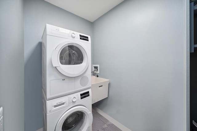 laundry area with stacked washer / dryer, laundry area, a sink, and baseboards