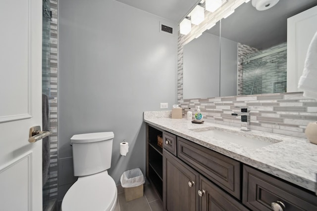 bathroom featuring toilet, visible vents, vanity, a tile shower, and decorative backsplash