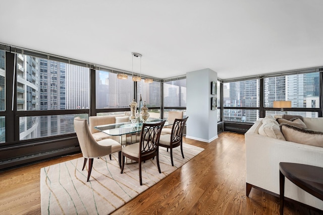 dining area featuring light wood-type flooring, a view of city, baseboards, and a wall of windows