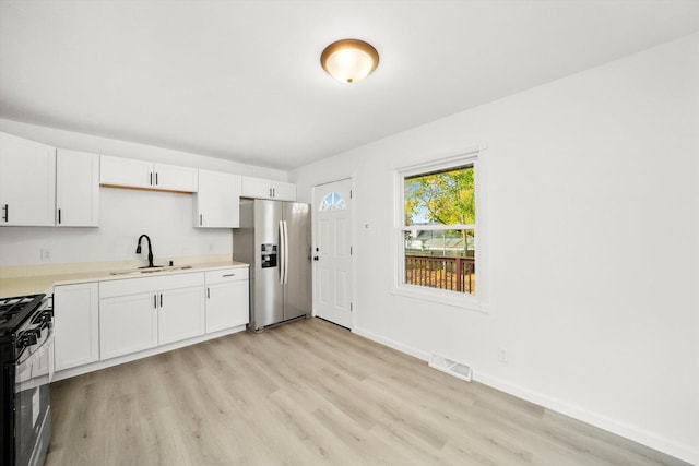 kitchen featuring a sink, white cabinetry, light countertops, stainless steel refrigerator with ice dispenser, and range with gas cooktop