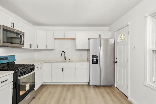 kitchen featuring stainless steel appliances, a sink, white cabinetry, light wood-style floors, and light countertops