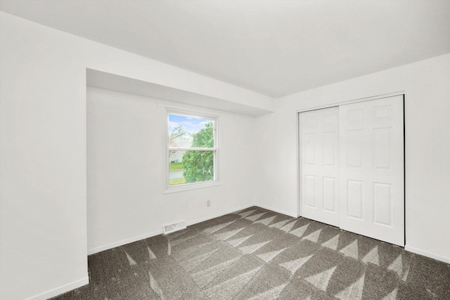 unfurnished bedroom featuring dark colored carpet, a closet, visible vents, and baseboards