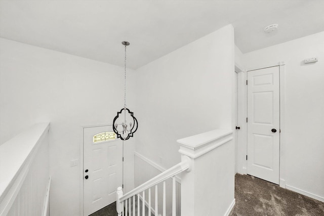 corridor with a chandelier, baseboards, dark colored carpet, and an upstairs landing