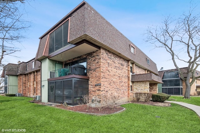 view of property exterior featuring a shingled roof, mansard roof, a lawn, and brick siding