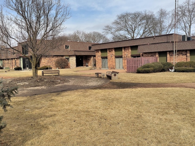 mid-century modern home with a shingled roof, brick siding, a front lawn, and mansard roof