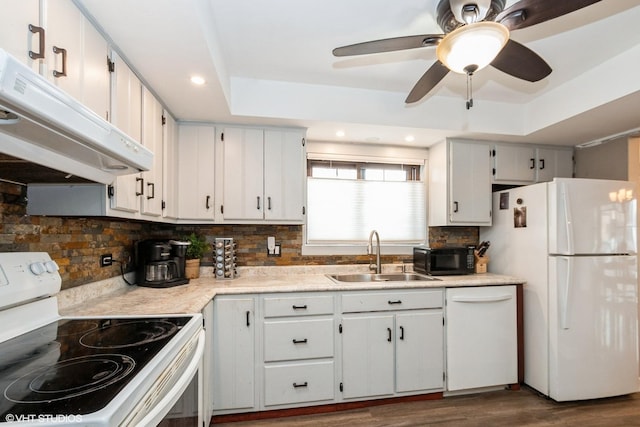 kitchen with a raised ceiling, white appliances, a sink, and under cabinet range hood