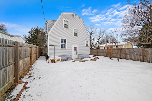 snow covered back of property featuring a fenced backyard and a gambrel roof