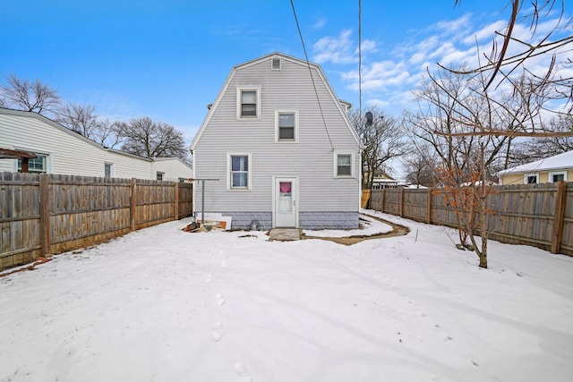 snow covered back of property featuring entry steps, a fenced backyard, and a gambrel roof