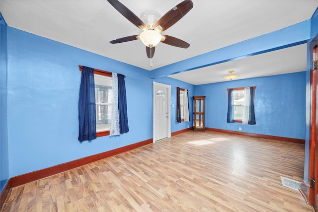 empty room with light wood finished floors, a ceiling fan, visible vents, and baseboards