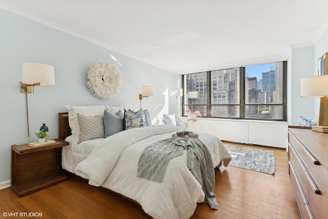 bedroom with a view of city, crown molding, and light wood finished floors