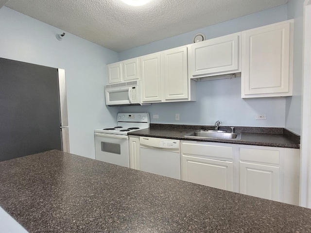 kitchen with white appliances, dark countertops, a sink, and white cabinetry