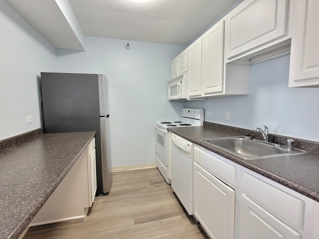 kitchen with light wood finished floors, dark countertops, white cabinetry, a sink, and white appliances