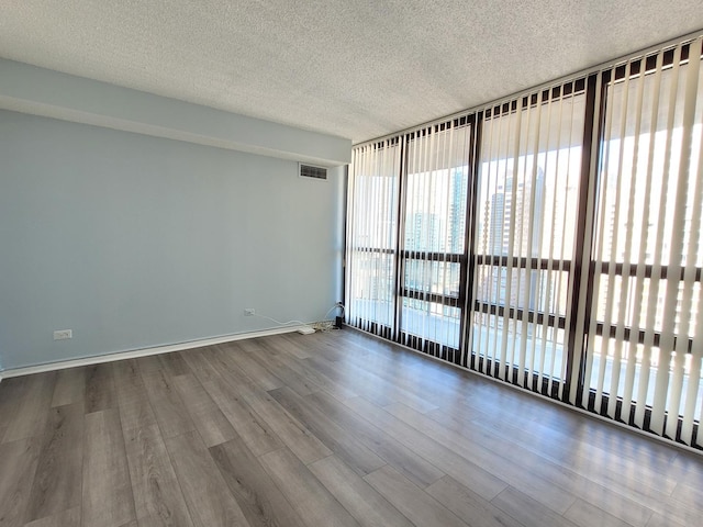 unfurnished room featuring a textured ceiling, wood finished floors, visible vents, baseboards, and expansive windows