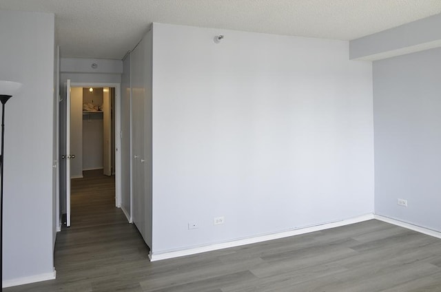 empty room featuring a textured ceiling, wood finished floors, and baseboards