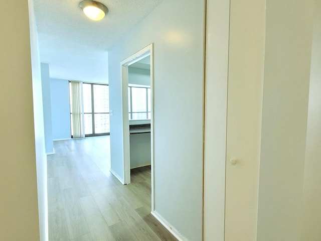 hall featuring a textured ceiling, light wood finished floors, and baseboards