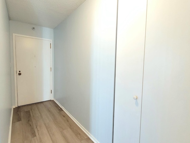 hallway with light wood-type flooring, a textured ceiling, and baseboards