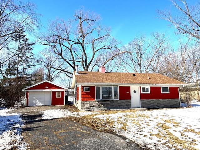 ranch-style home with a detached garage, an outdoor structure, stone siding, driveway, and a chimney