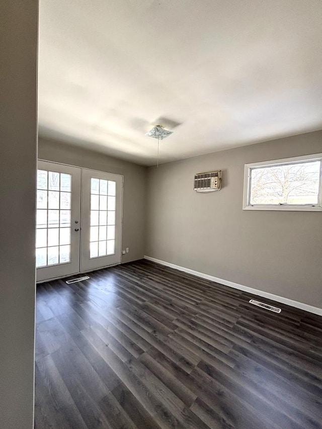 empty room with visible vents, baseboards, french doors, dark wood-style floors, and a wall mounted air conditioner