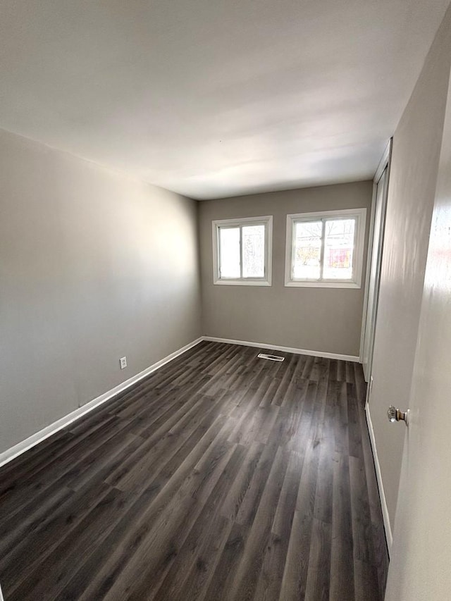 empty room with dark wood-style flooring and baseboards