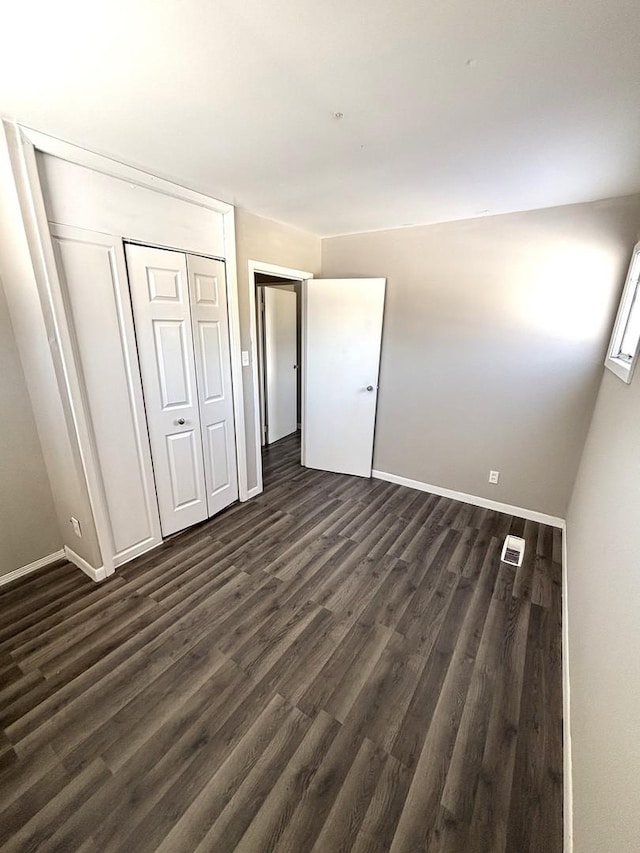 unfurnished bedroom featuring dark wood-style floors, baseboards, visible vents, and a closet