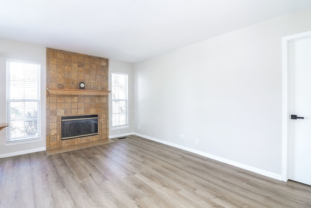 unfurnished living room with a tile fireplace, light wood-style flooring, and baseboards