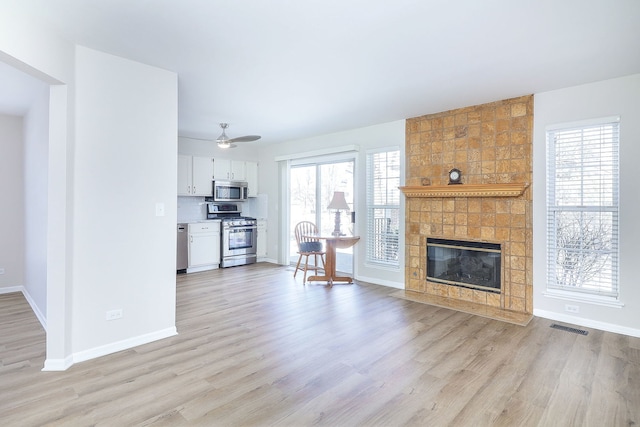 unfurnished living room with light wood-type flooring, a fireplace, visible vents, and baseboards