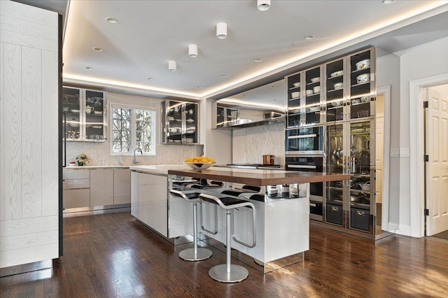 kitchen with wooden counters, dark wood finished floors, oven, glass insert cabinets, and backsplash