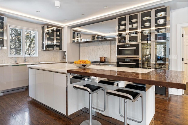 kitchen with decorative backsplash, glass insert cabinets, dark wood-style flooring, and a sink