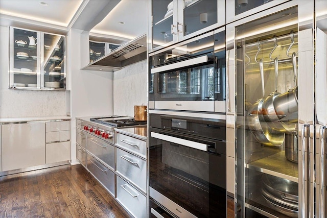 kitchen featuring extractor fan, glass insert cabinets, dark wood-style flooring, and stainless steel gas cooktop