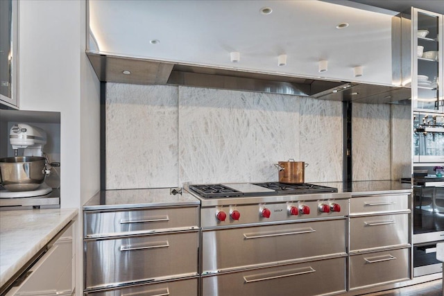 kitchen featuring stovetop, glass insert cabinets, extractor fan, and light countertops