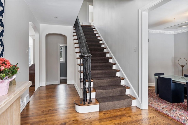 foyer entrance with baseboards, arched walkways, wood finished floors, and stairway