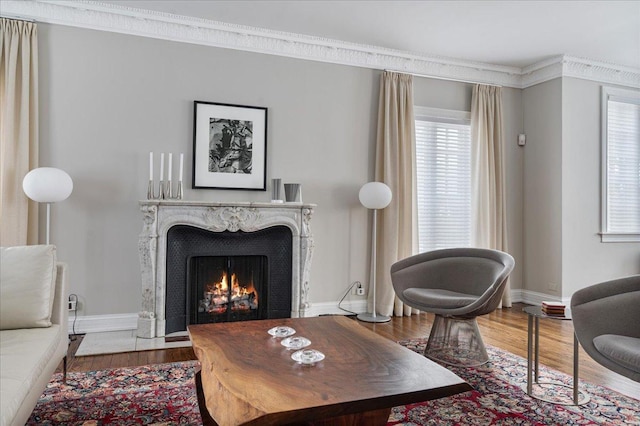 living room featuring wood finished floors, baseboards, a high end fireplace, and ornamental molding