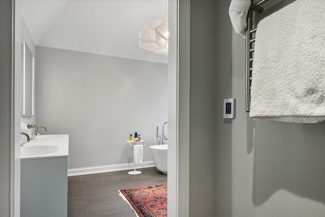 full bath with lofted ceiling, a sink, double vanity, baseboards, and a soaking tub