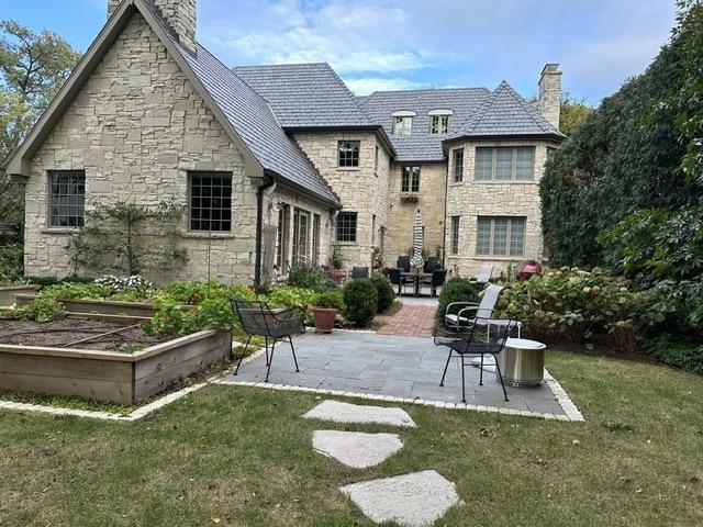 rear view of property with a patio area, a high end roof, a lawn, and a chimney