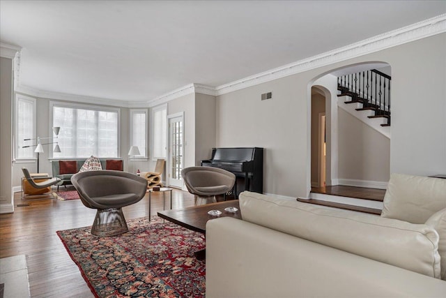 living room featuring visible vents, ornamental molding, wood finished floors, arched walkways, and stairs