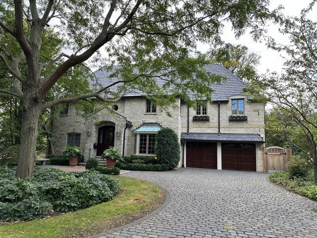 french country inspired facade featuring decorative driveway, stone siding, and an attached garage