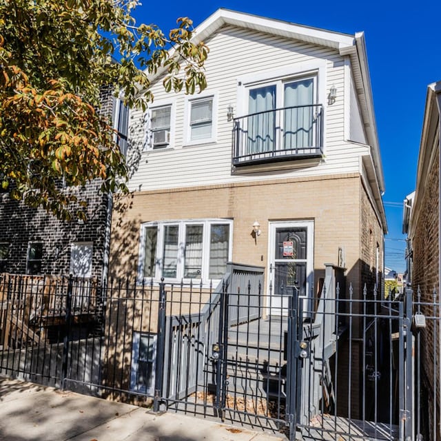 townhome / multi-family property featuring a fenced front yard, brick siding, a gate, a balcony, and cooling unit