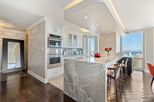 kitchen featuring wood finished floors, white cabinetry, a kitchen breakfast bar, light stone countertops, and glass insert cabinets