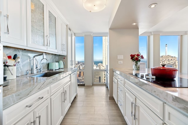 kitchen featuring black electric stovetop, glass insert cabinets, white cabinets, a sink, and a wall of windows