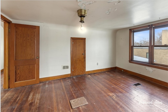 spare room with dark wood-type flooring, visible vents, and baseboards