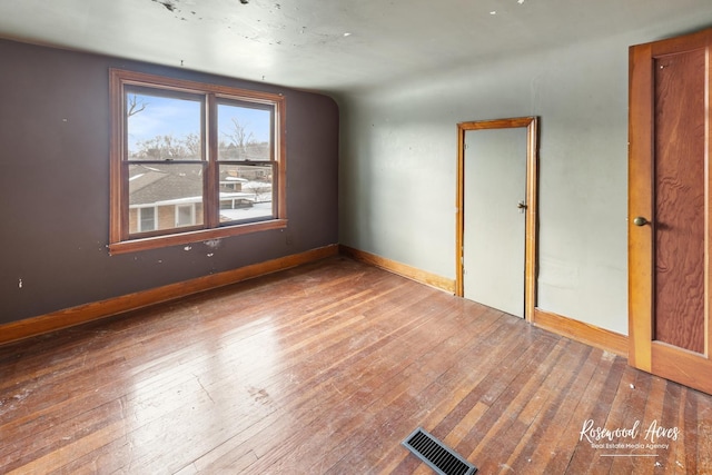 empty room with wood finished floors, visible vents, and baseboards