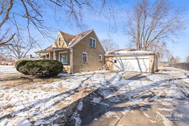 snow covered property with a garage, fence, and brick siding