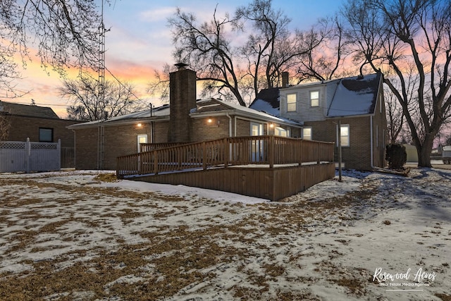 snow covered house featuring brick siding, a chimney, and a wooden deck