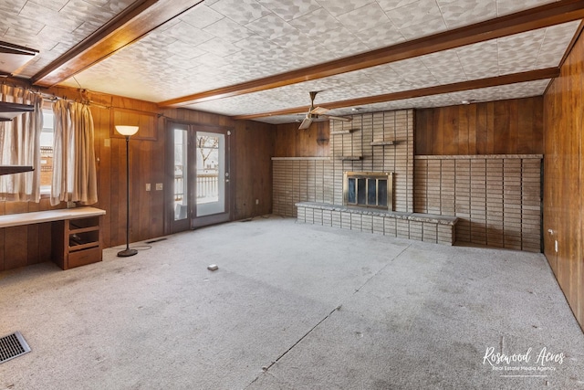 unfurnished living room featuring carpet, beam ceiling, visible vents, a brick fireplace, and wood walls