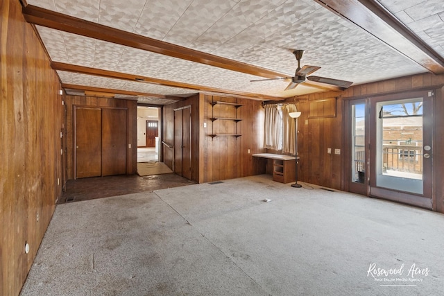 unfurnished room featuring wood walls, dark colored carpet, and beam ceiling