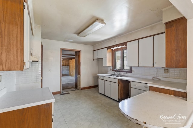 kitchen featuring tasteful backsplash, light countertops, white cabinetry, a sink, and baseboards