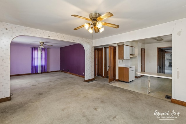 unfurnished living room with wallpapered walls, arched walkways, baseboards, light colored carpet, and ceiling fan