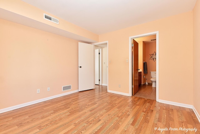 unfurnished bedroom with baseboards, visible vents, ensuite bath, and light wood finished floors