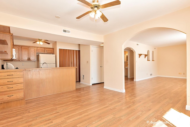 unfurnished living room with arched walkways, visible vents, ceiling fan, light wood-type flooring, and baseboards