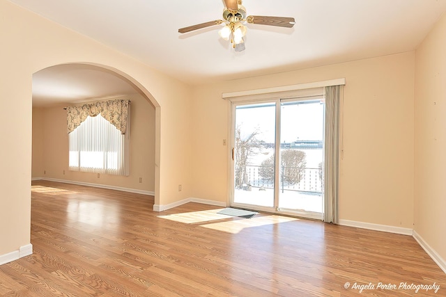 empty room featuring light wood-type flooring, baseboards, and arched walkways